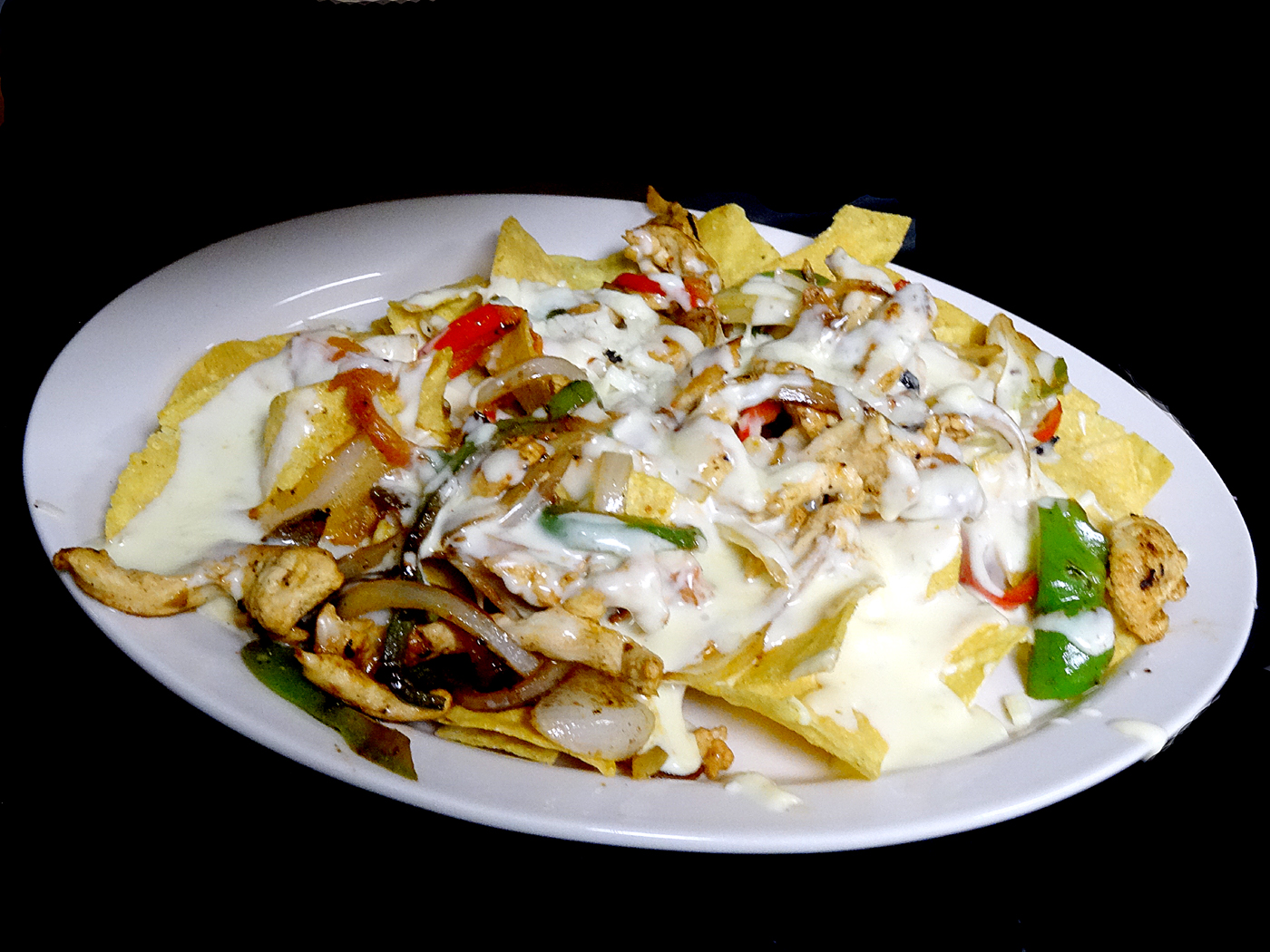 Nachos de fajita: tortilla chips under grilled chicken, red and green peppers and onions, covered in white cheese dip.