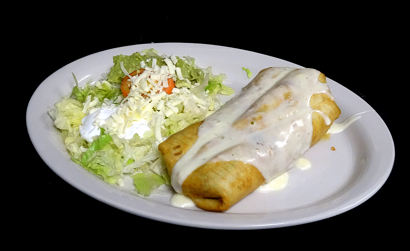 A fried flour tortilla under white cheese sauce, beside a guacamole salad with shredded cheese and sour cream.