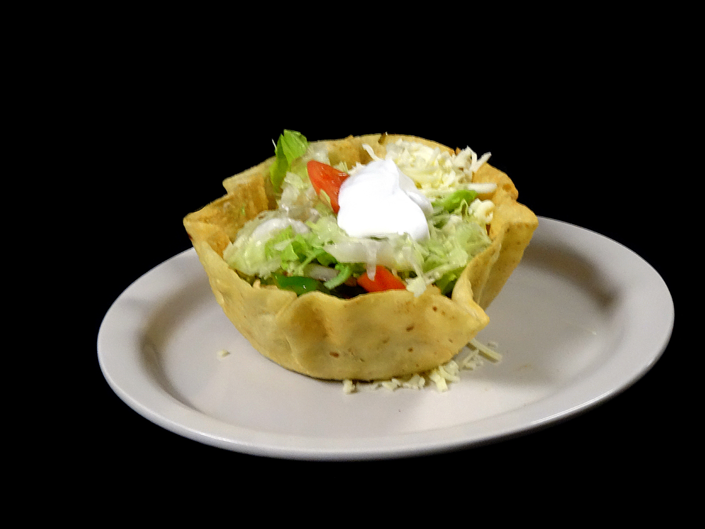 A fried tortilla bowl filled with lettuce, tomato, green pepper, shredded cheese and sour cream.